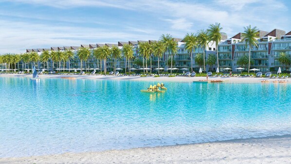 A resort pool with clear blue water, surrounded by palm trees and a row of hotel buildings.