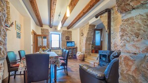 A cozy living room with stone walls, a fireplace, a dining area with a table and chairs, and a leather sofa.