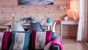 A cozy room with a wooden wall, a dining table set with glasses and a bottle, and a sofa with patterned cushions.