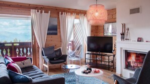 A cozy living room with a sofa, chairs, a TV, a fireplace, and a view of the mountains.