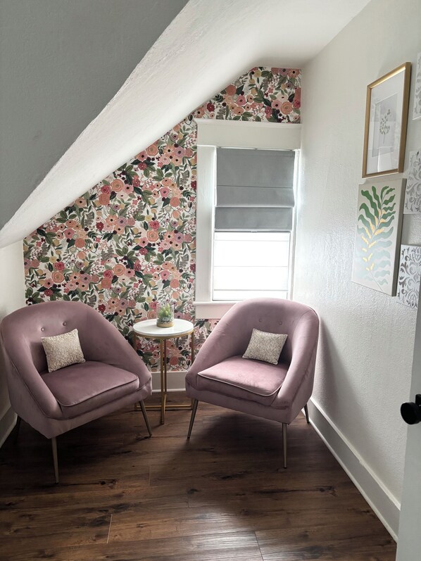 A cozy room with two pink armchairs, a small round table, and a floral-patterned wall.