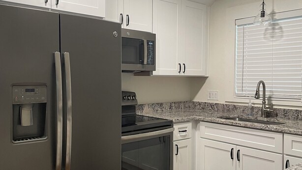 A modern kitchen with white cabinets, stainless steel appliances, and granite countertops.