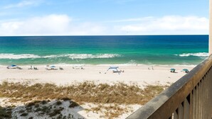 Ein Strand mit klarem türkisblauem Wasser, einem sandigen Ufer und einer Holzterrasse mit Blick auf den Ozean.