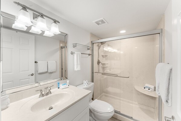 A modern bathroom with a large mirror, a sink, a toilet, and a glass-enclosed shower. - Fall Break Getaway at PP B2-608 (Panama City Beach)