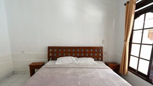 Un dormitorio con cabecera de madera, dos almohadas blancas, cama con cubrecama a rayas, mesita de noche, mesa de madera y ventana con cortinas.