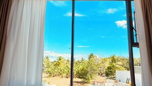 Een kamer met een grote schuifglazen deur die leidt naar een balkon met vrij uitzicht op palmbomen en een hek.