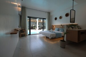 A modern hotel room with a bed, a desk, a chair, a potted plant, and a view of the outdoor area.