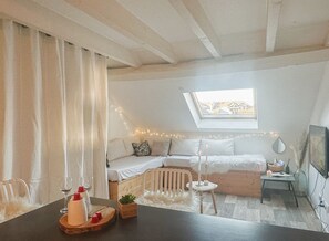 A cozy bedroom with a loft bed, a skylight, a small table with candles, and a view of the countryside.