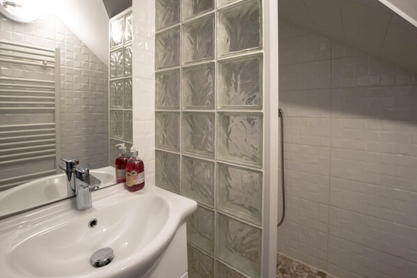 A bathroom with a white sink, chrome faucet, and a mirror. There are two bottles of red liquid on the sink. The walls are tiled with a white and green pattern.