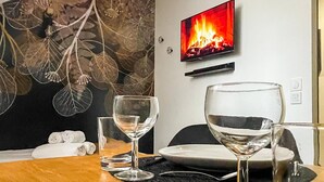 Une chambre d’hôtel avec une table à manger dressée pour deux personnes, deux verres à vin, une assiette et un tableau représentant un feu sur le mur.
