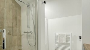 Une salle de bain moderne avec une douche à parois de verre, des toilettes blanches et un porte-serviettes.