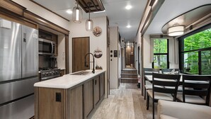A modern kitchen with stainless steel appliances, a central island, and a dining area with a view. - Luxury Creekside Retreat: RV in Gatlinburg,Tn (Gatlinburg)