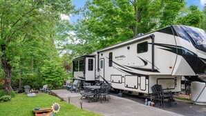 A Sanibel wide-body RV parked in a campsite with outdoor seating and a sunflower decoration. - Luxury Creekside Retreat: RV in Gatlinburg,Tn (Gatlinburg)
