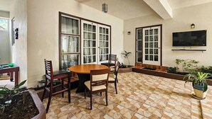 Comedor con una mesa redonda y sillas, ventanas amplias, televisor de pantalla plana y plantas en macetas.