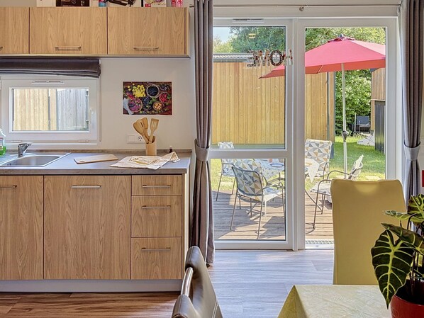 A modern kitchen with wooden cabinets, a large window, and a dining area with outdoor seating.