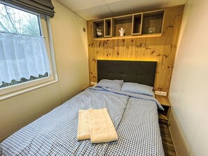 Un dormitorio con cama, una ventana con cortinas, una estantería con adornos y un cabecero.