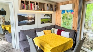 Una habitación acogedora con un sofá gris, una mesa cubierta con mantel amarillo y una estantería llena de libros.