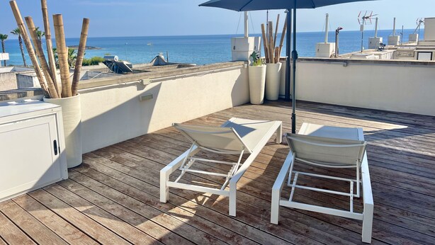 A wooden deck with two white lounge chairs and a blue umbrella, overlooking a body of water. - TSG 4 (Apartment + Extra Overview Terrace) (Ugento)