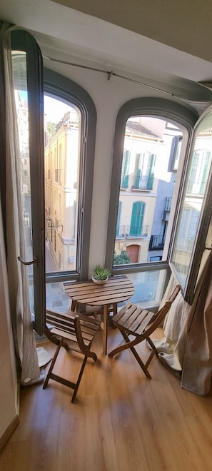 A room with a wooden table and chairs, a potted plant, and a view of buildings through large windows.