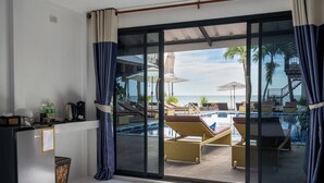 Una stanza con una porta vetrata che dà su una zona piscina, con lettini e ombrelloni.
