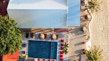 Un área de piscina en la azotea con una piscina rectangular, rodeada de sillas de descanso rojas y una terraza blanca.