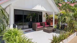 Una casa moderna con fachada blanca, grandes ventanales y un porche cubierto con mobiliario exterior.