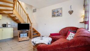 A living room with a red sofa, wooden staircase, flat-screen TV, and a small table with a decorative tablecloth. - Apartment 'Fewo 12 - Halbinsel Darss - Ostsee' with Private Terrace, Shared Garden and Wi-Fi (Wieck am Darß)