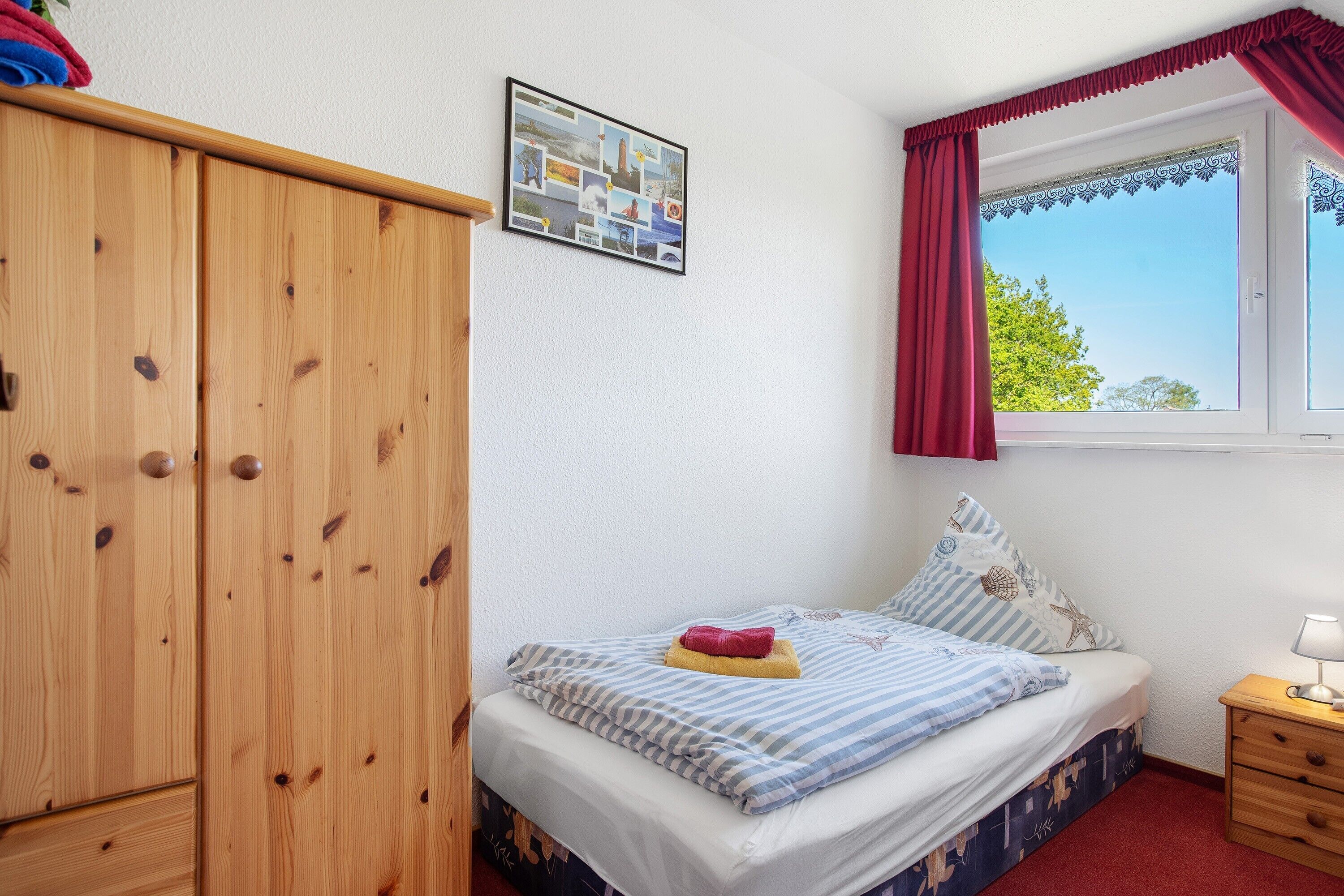 Ein Schlafzimmer mit einem Bett, einem Holzschrank, einem Fenster mit Vorhängen, einem Nachttisch und einer an der Wand befestigten Fotocollage.