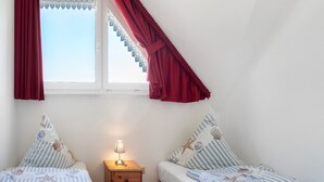 A bedroom with two beds, a nightstand with a lamp, and a window with curtains. - Apartment 'Fewo 12 - Halbinsel Darss - Ostsee' with Private Terrace, Shared Garden and Wi-Fi (Wieck am Darß)