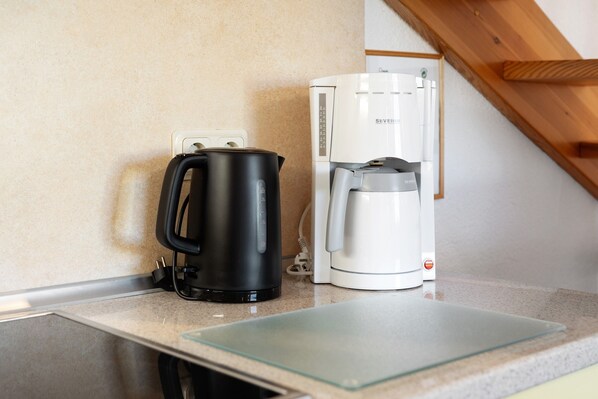 A kitchenette with a black electric kettle and a white coffee maker on a countertop.