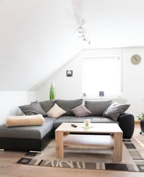 Ein modernes Wohnzimmer mit einer grauen Couch, einem Holztisch und einem großen Fenster.