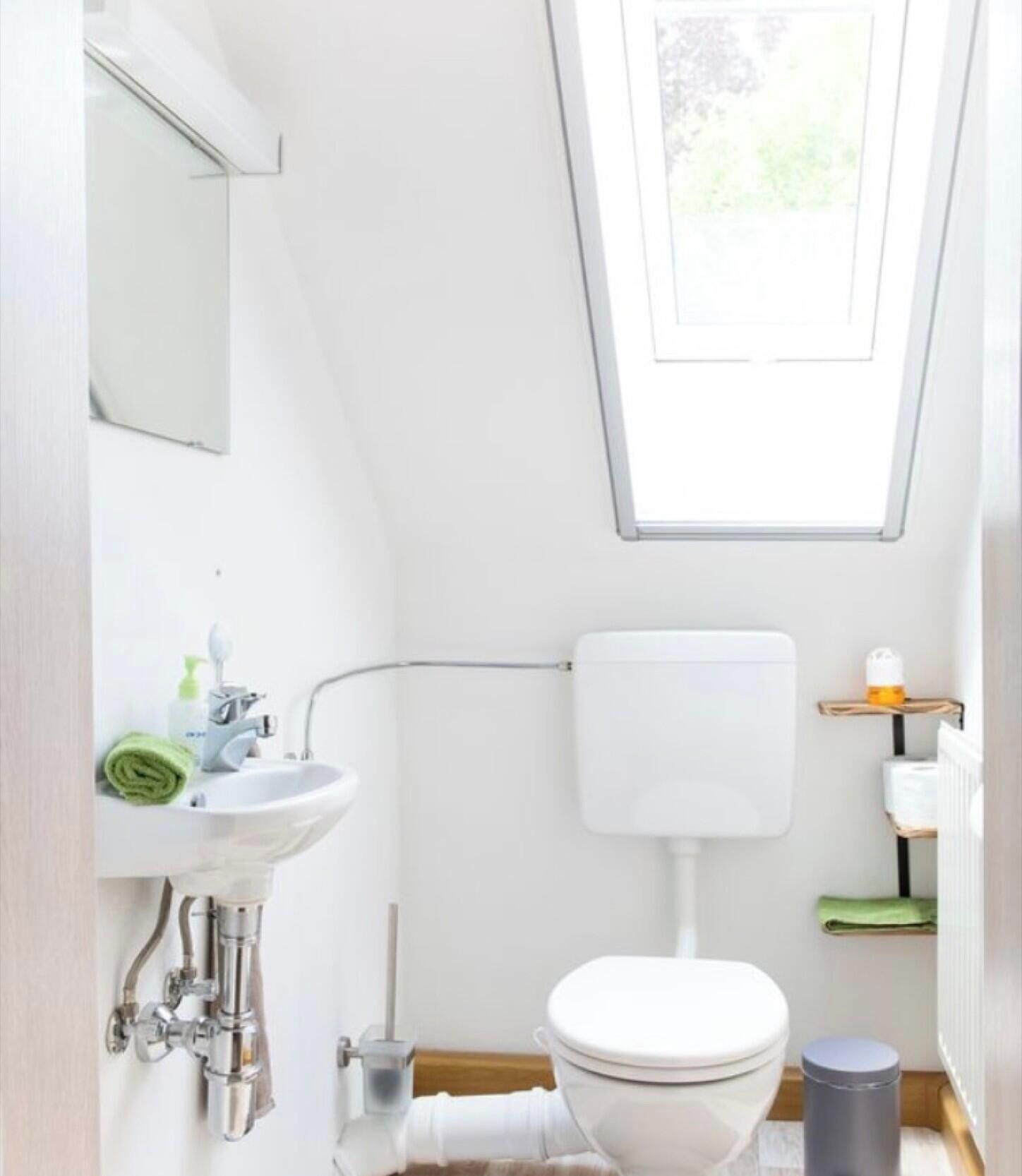 A bathroom with a skylight, toilet, sink, and a towel.