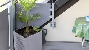 Ein Balkon mit einem Blumentopf, einem Tisch mit grüner Tischdecke und einem Fenster mit Blick auf ein Gebäude.