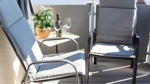 Ein Balkon mit zwei Stühlen, einem kleinen Tisch, einer Pflanze, einer Flasche und zwei Gläsern.