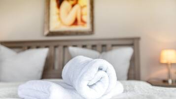 A neatly made bed with a rolled white towel, a wooden headboard, and a framed picture on the wall.