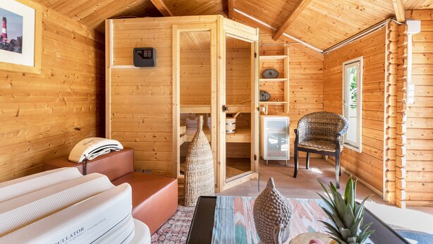 Interior de una cabaña de madera con sauna, zona de estar y vistas al exterior.