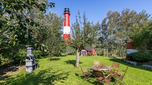 Un jardín con un faro rojo y blanco, una mesa de madera con sillas y un pequeño edificio rojo.