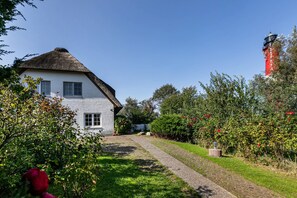 A white house with a thatched roof, a red and black lighthouse, and a gravel path leading to the house. - Apartment 'Südwest' with Shared Terrace, Private Garden and Wi-Fi (Pellworm)