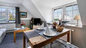 A cozy loft-style room with a dining area, a window with a view, a sailboat model, and a lamp. - Apartment 'Südost' with Shared Terrace, Private Garden and Wi-Fi (Pellworm)