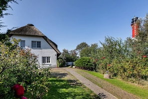 Ett vitt hus med ett halmtak, ett rött och svart fyrtorn och en grusgång som leder fram till huset.