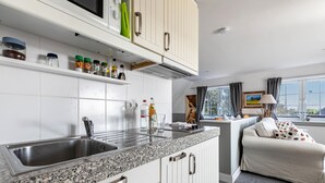 A kitchen with a granite countertop, stainless steel sink, white cabinets, and a window with curtains. - Apartment 'Südost' with Shared Terrace, Private Garden and Wi-Fi (Pellworm)
