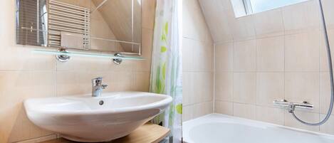 A modern bathroom with a large bathtub, a glass shelf with a sink, and a shower with a hose.