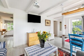 Ein modernes Wohnzimmer mit einem Flachbildfernseher, einer Holzkommode, einem blauen Sessel und einer Vase mit Blumen.