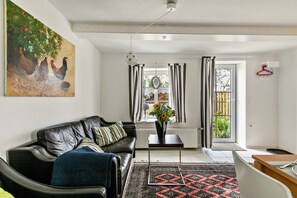 Un salon avec un canapé, une table basse, un tableau, un vase de fleurs et une vue par la fenêtre.