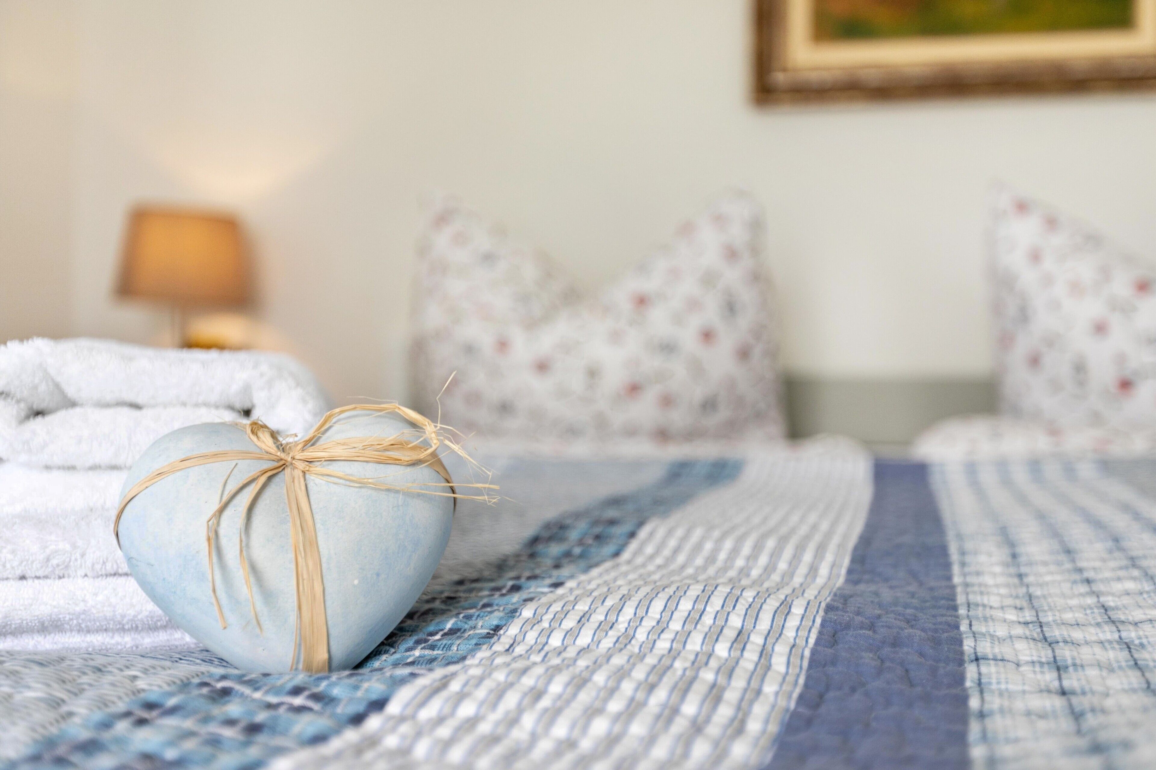 Una cama con un edredón azul, un objeto con forma de corazón atado con hilo, y almohadas estampadas.