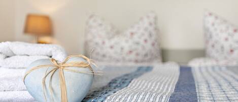 Una cama con un edredón azul, un objeto con forma de corazón atado con hilo, y almohadas estampadas.