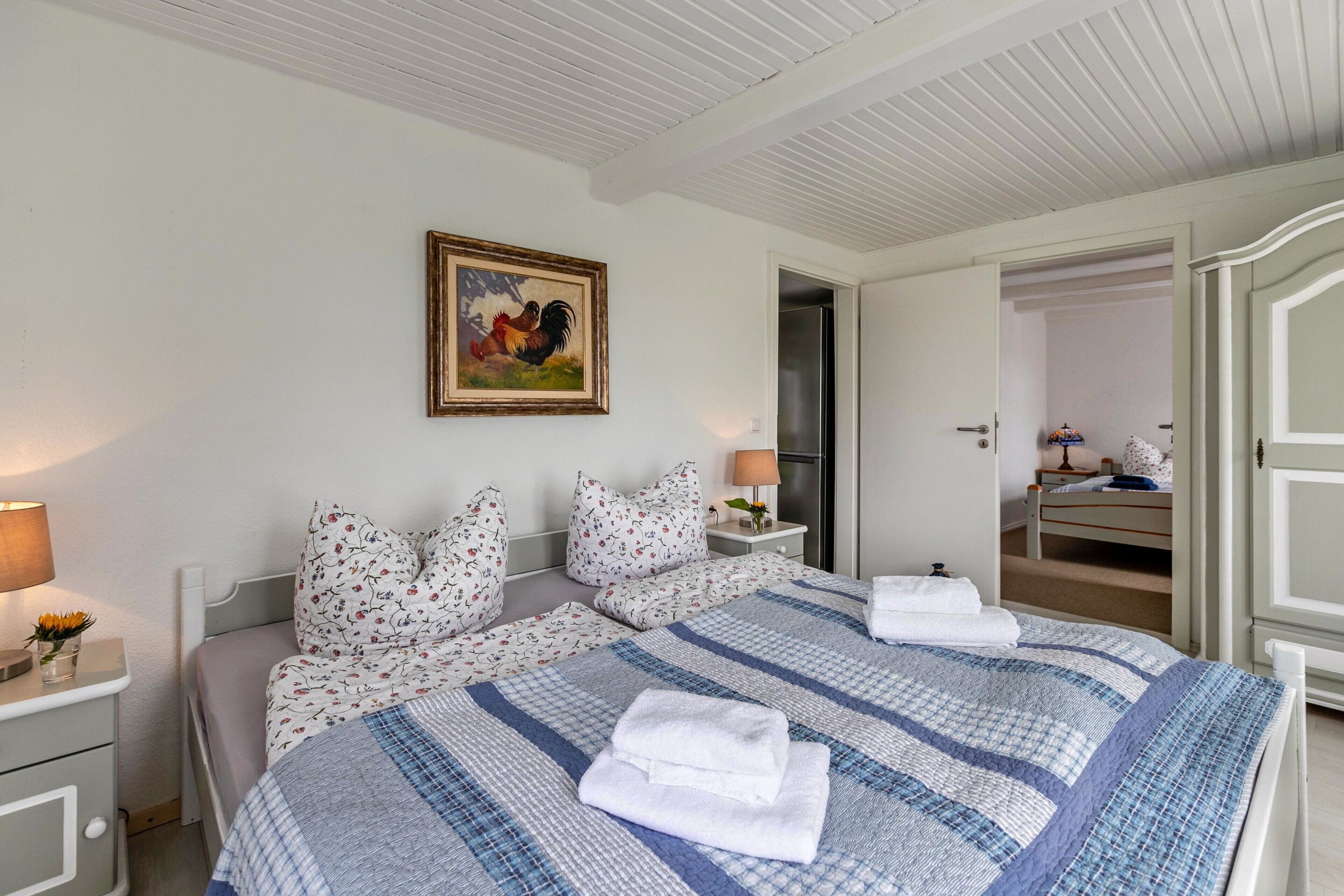 A bedroom with a bed, pillows, a nightstand, a lamp, a painting, and a wardrobe.