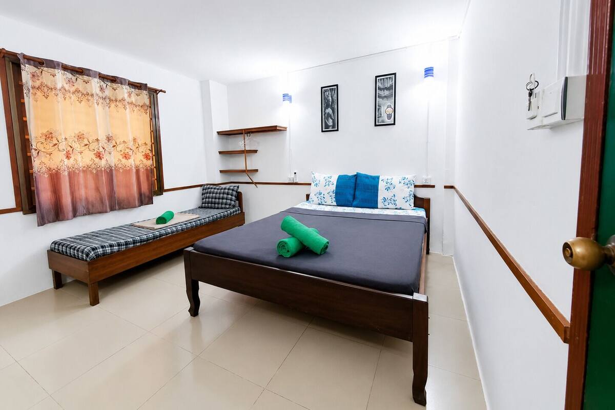 Ein Schlafzimmer mit einem Bett, einem Sofa, einem Vorhang, einem an der Wand befestigten Regal und gerahmten Bildern.