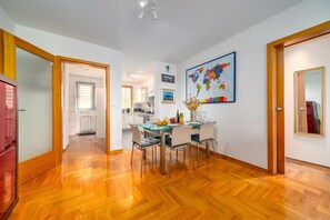 A modern kitchen with white cabinets, a dining table with chairs, and a world map artwork on the wall.