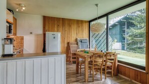 Une cuisine moderne avec un lambris en bois, un coin repas avec une table et des chaises en bois, et une grande fenêtre offrant une vue sur l’extérieur.
